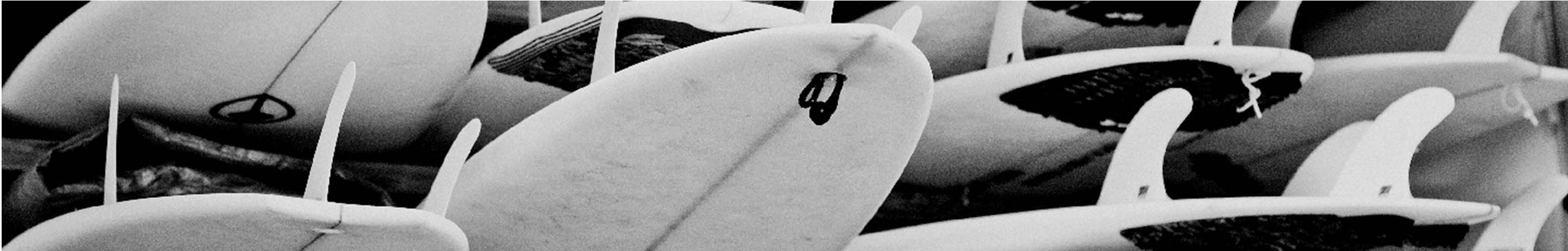 Black and white close-up of multiple surfboards with fins visible, stacked together.